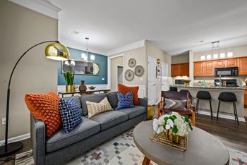 a living room and kitchen with a grey couch and orange and blue pillows
